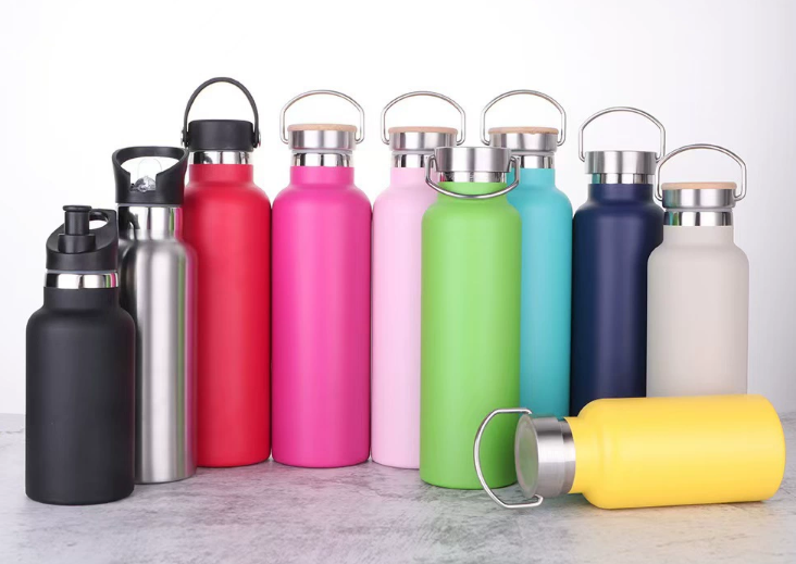 a shiny stainless steel water bottle standing in a lush green forest