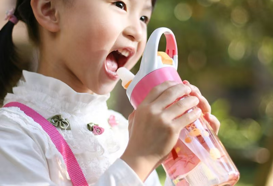 A happy toddler drinking from a durable, colorful plastic water bottle in a park