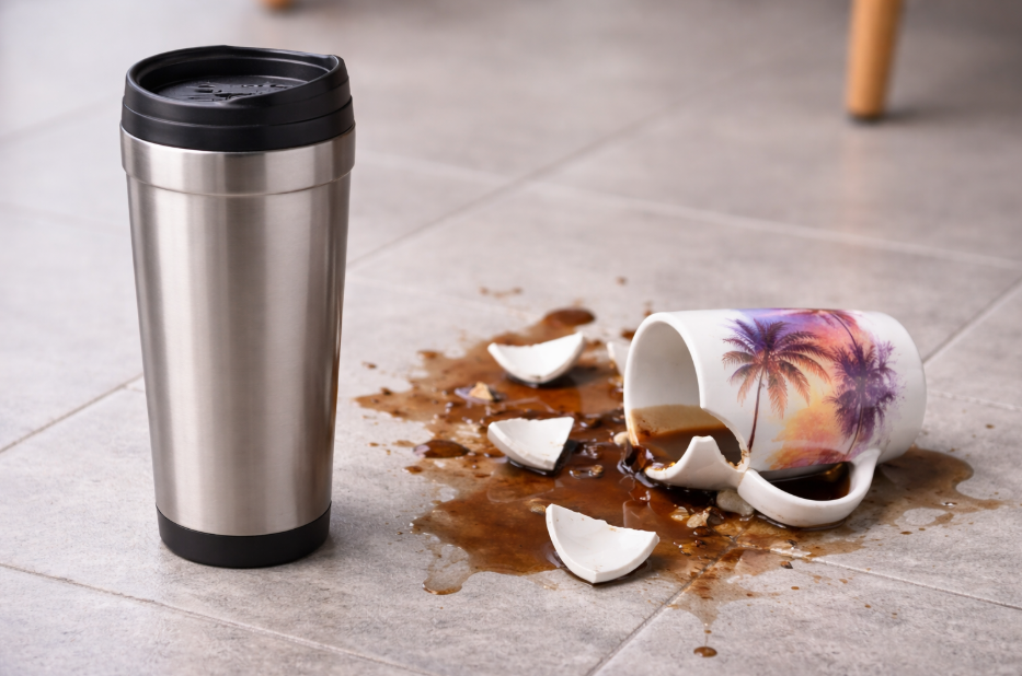 A stainless steel travel mug unscratched next to a shattered ceramic mug on the floor