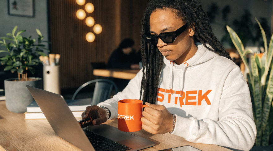 A person at their desk using a branded mug, a branded USB drive, and wearing a branded hoodie