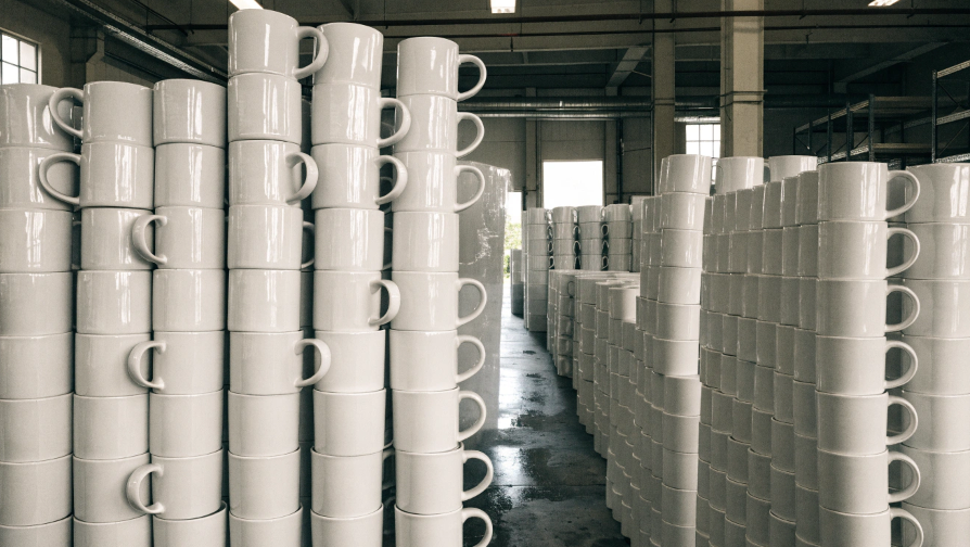 A warehouse filled with stacks of blank white coffee mugs ready for customization